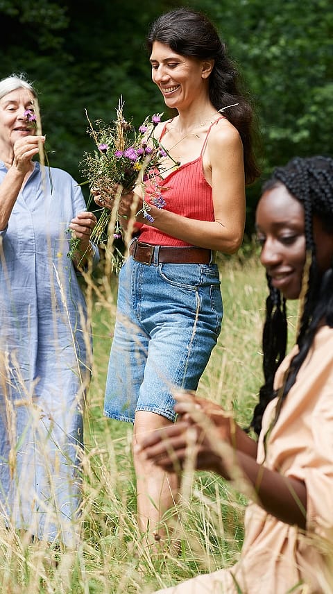 Tri ženske različnih starosti skupaj nabirajo rože na travniku.